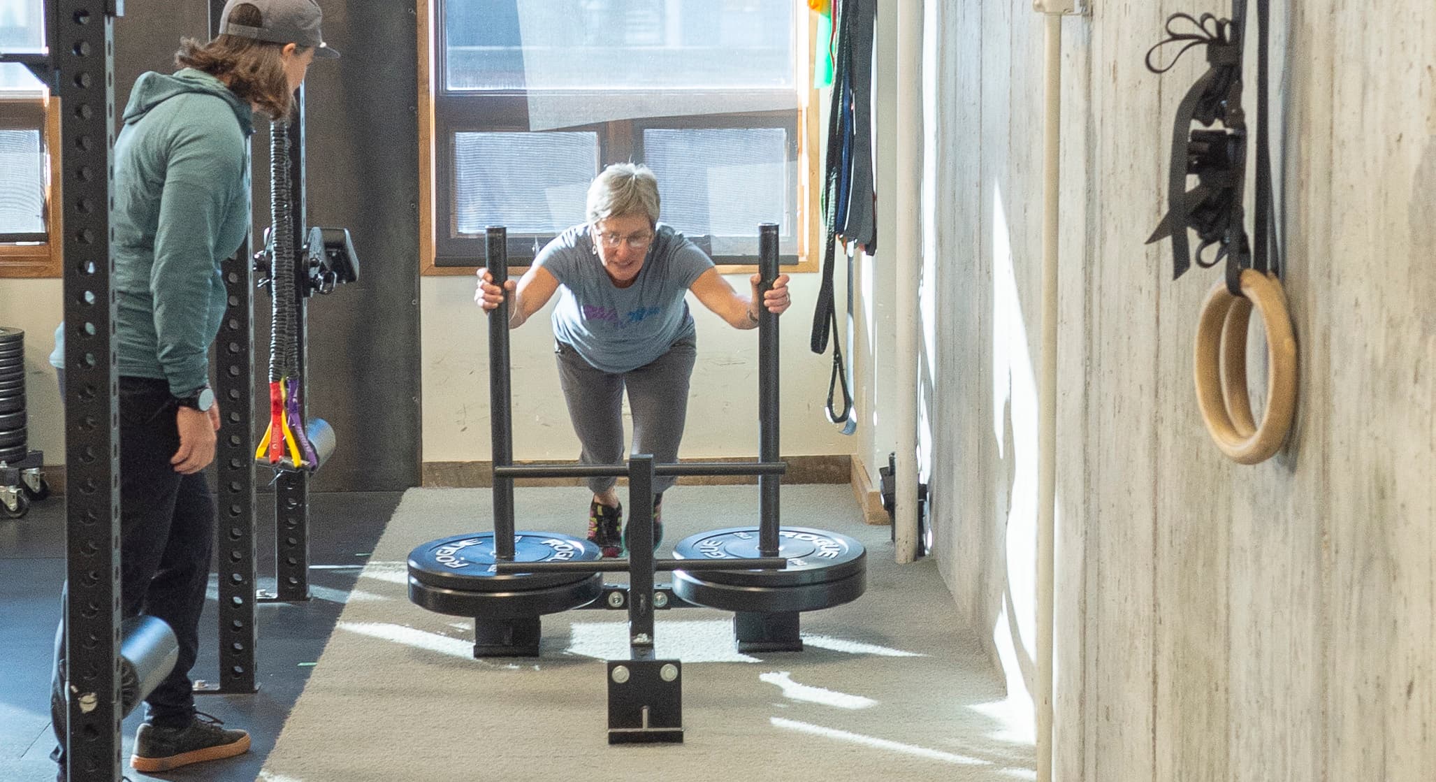 gym member pushing sled with coach